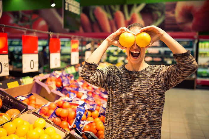 women holds oranges over her eyes at supermarket