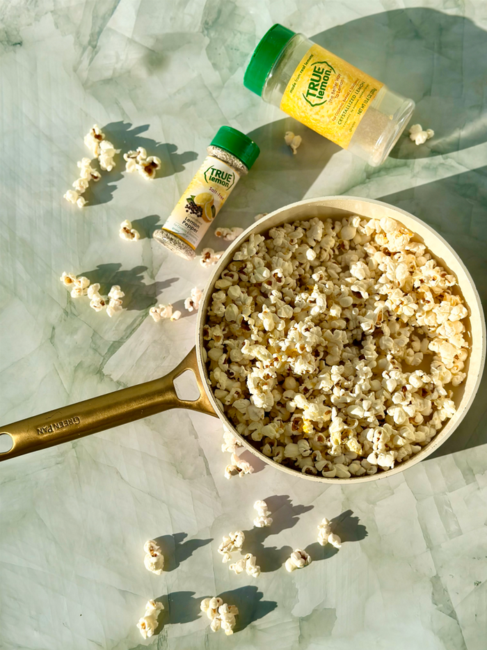 Picture of seasoned popcorn in a pan with True Citrus spice blend in the back ground.