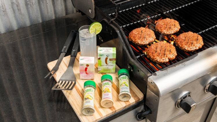 Backyard BBQ with hamburgers on the grill. Next to the grill are True Lemon Spice Blends for cooking and seasoning, and boxes of True Lemon Fruit Infusion.  