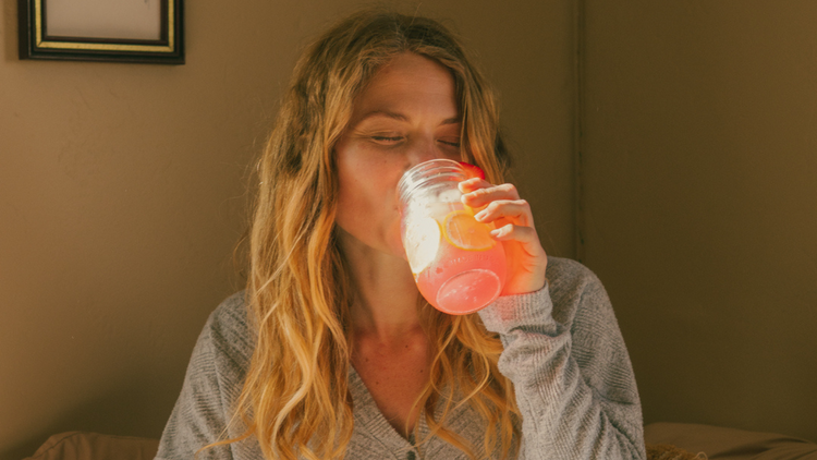 Image of a woman drinking a glass of water with True Lemon Strawberry Lemonade.