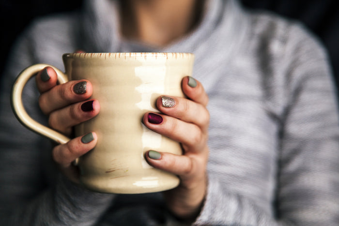 Up close view of woman holding coffee mug with silver painted nails