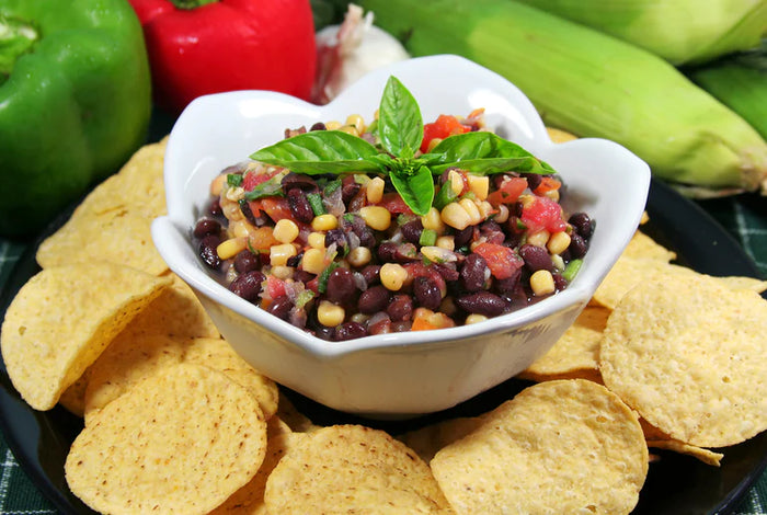 Bowl of lime corn and black bean salsa surrounded by tortilla chips.