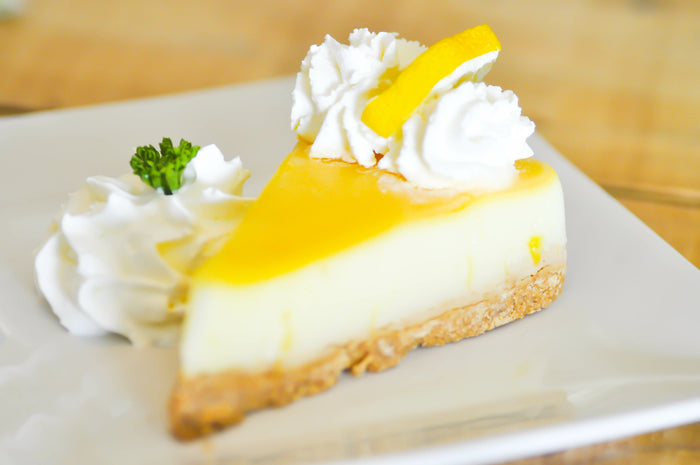 Lemon cheesecake on a plate, topped with lemon curd, whipped cream, and a lemon slice.