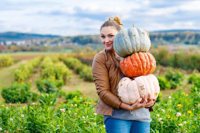 women smiles and holds a few pumpkins