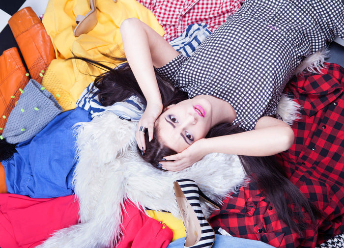 women lays in a pile of clothes with her hands on her head