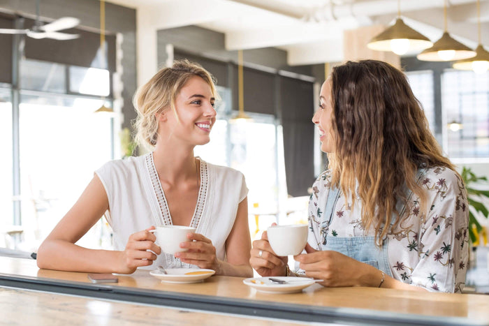 two friends smile while drinking in a coffee shop together
