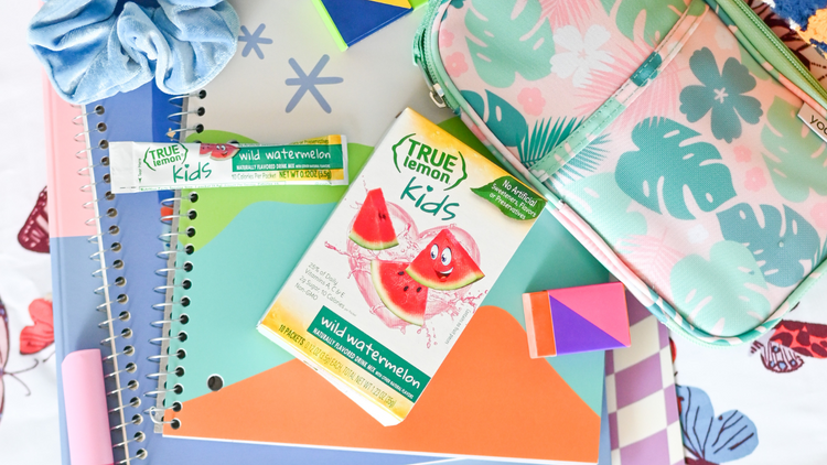 A box of True Lemon Kids Wild Watermelon is on top of an assortment of school supplies such as a pencil pouch and notebooks. 