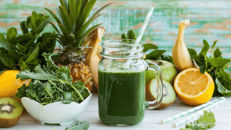 A green smoothie is at the center of a display of green and yellow vegetables.