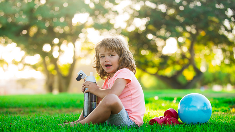 Little girl sitting on a lawn during the summer drinking a bottle of water. 