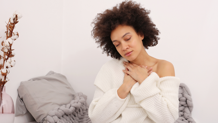 A woman meditating, breathing deeply with her hands on her chest. 
