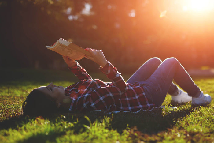 women reads a book while laying on the grass at a park
