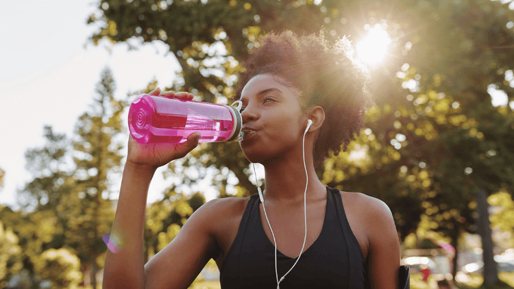 woman wearing earbuds is walking outside and drinking a True Lemon drink out of a water bottle