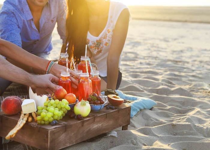 people share an assortment of juice and fruit on a beach