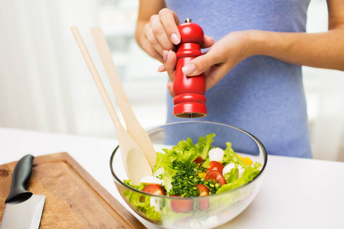 a woman puts salt on a fresh salad with salt grinder
