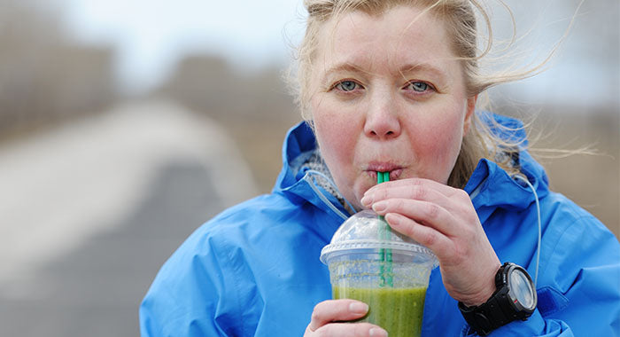 Woman outside in green jacket drinks green smoothie