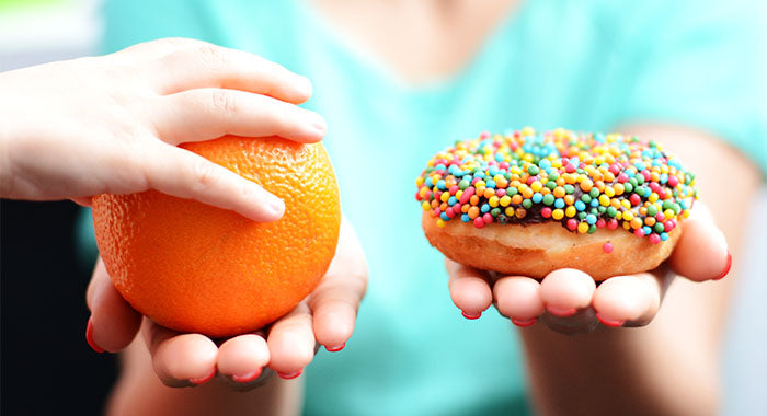 Woman in green shirt holding orange in one hand and a donut in the other