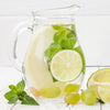 A large pitcher of limeade, made with True Lime Juice Mix. There are fresh lime slices, grapes, and mint leaves in the pitcher. 