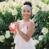 A young woman in a garden smiling and drinking a glass of True Lemon Raspberry Lemonade.