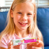 A young girl smiles and holds up a packet of True Lemon Kids Pink Lemonade.
